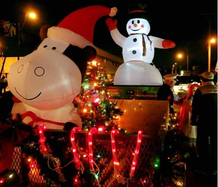Lighted blow-up snowman and cow with Santa hat and holiday lights on a trailer